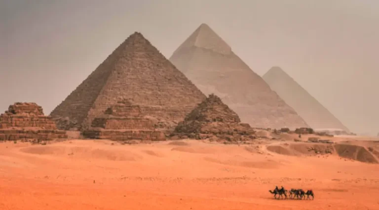 Pyramids of Giza at sunset with camel caravan in foreground crossing desert landscape