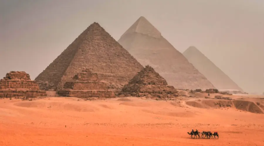 Pyramids of Giza at sunset with camel caravan in foreground crossing desert landscape